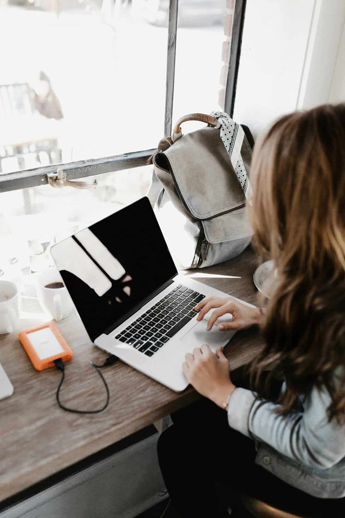 Reflecting on biblical Christian living, a woman working on a laptop at a coffee shop, with natural light and a peaceful environment, inspiring faith-based personal growth and spiritual development.