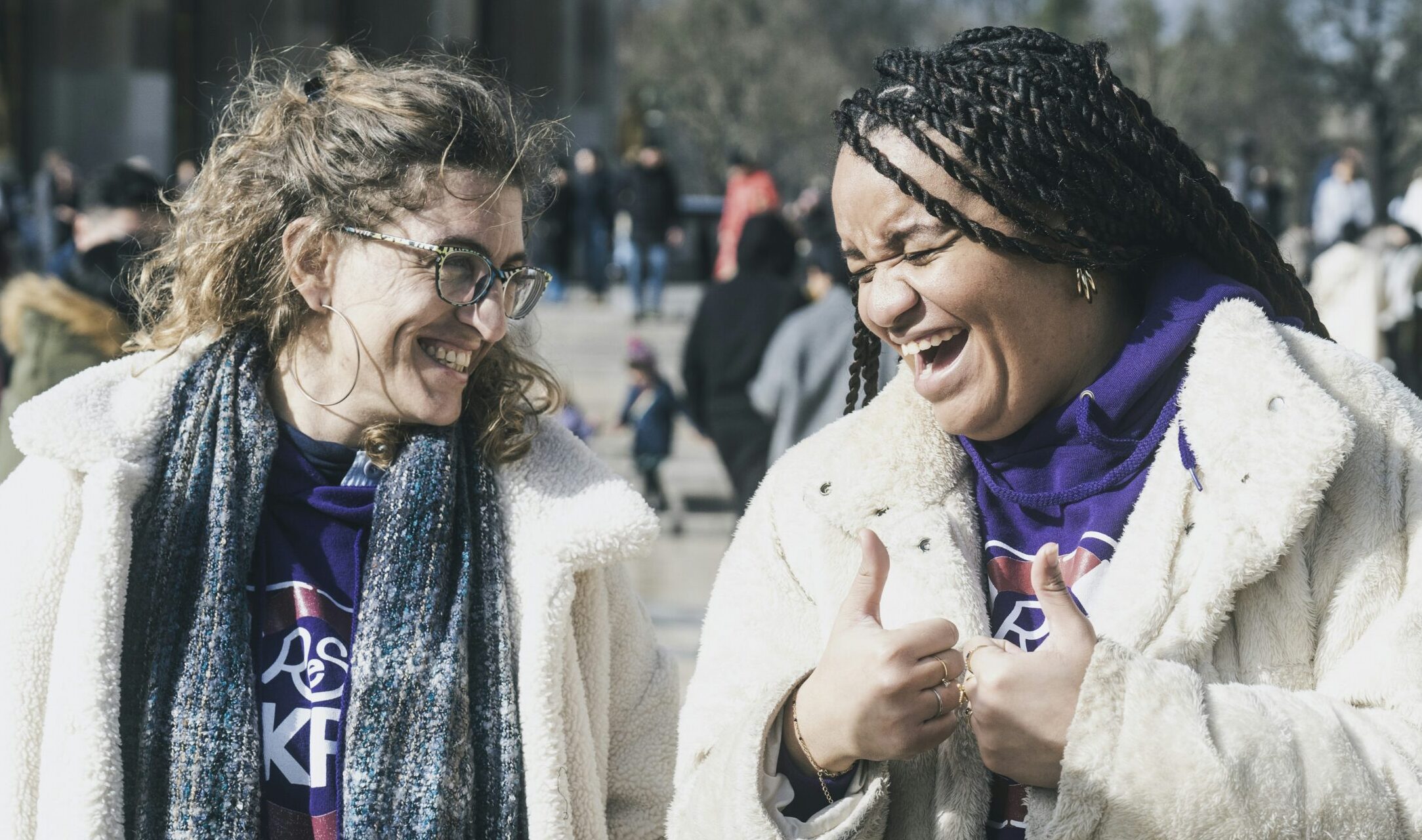 Two joyful women laughing together outdoors in winter coats, demonstrating authentic Christian fellowship and community connection in daily life