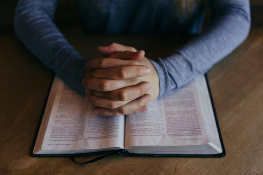 A person with an open Bible with his hands together as a sign of prayer, indicating that we need prayer for spiritual growth.