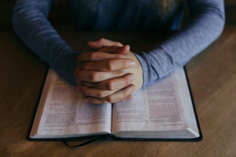 Hands folded in prayer over an open Bible, symbolizing how to pray to combat spiritual attacks.
