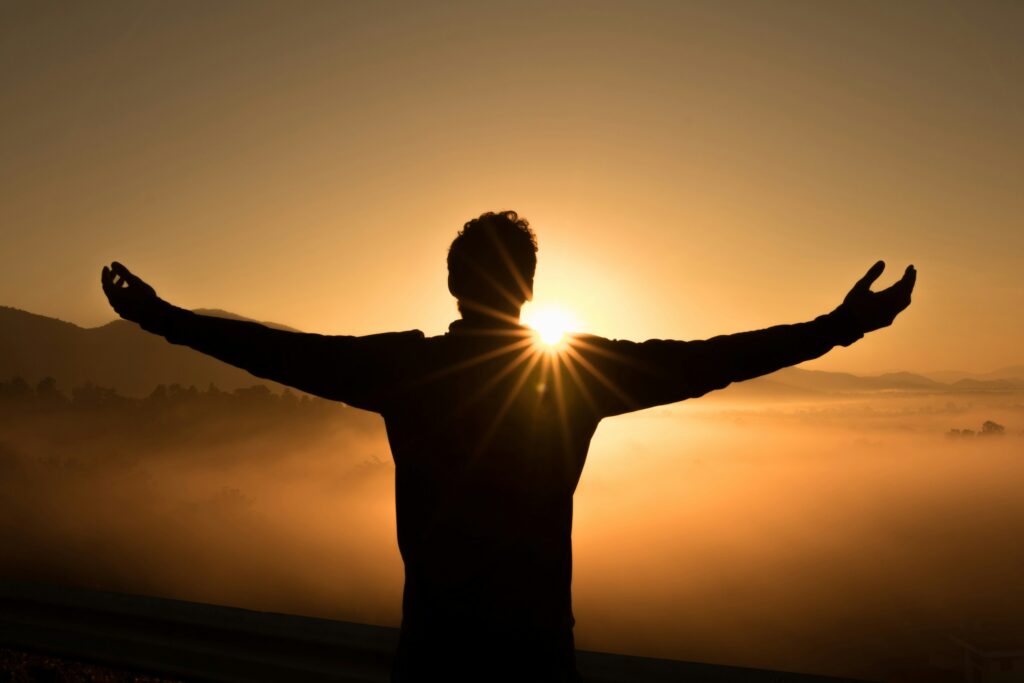 A picture of a man with his arms wide open, facing the sunset  on a hill, as an indication of spiritual growth.