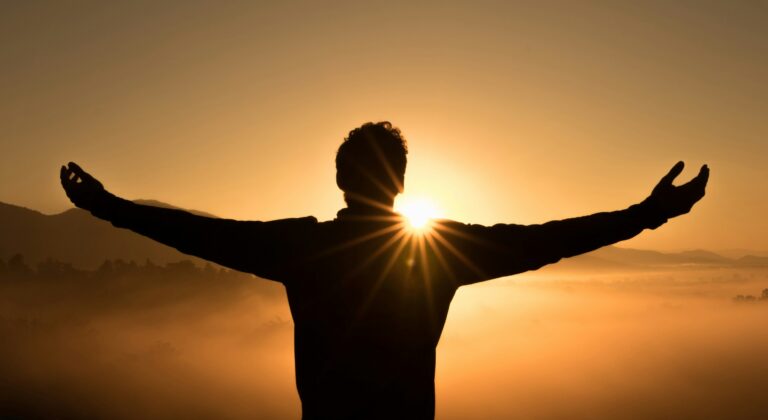 "Silhouette of person with arms raised toward golden sunrise expressing desire to change and spiritual growth"