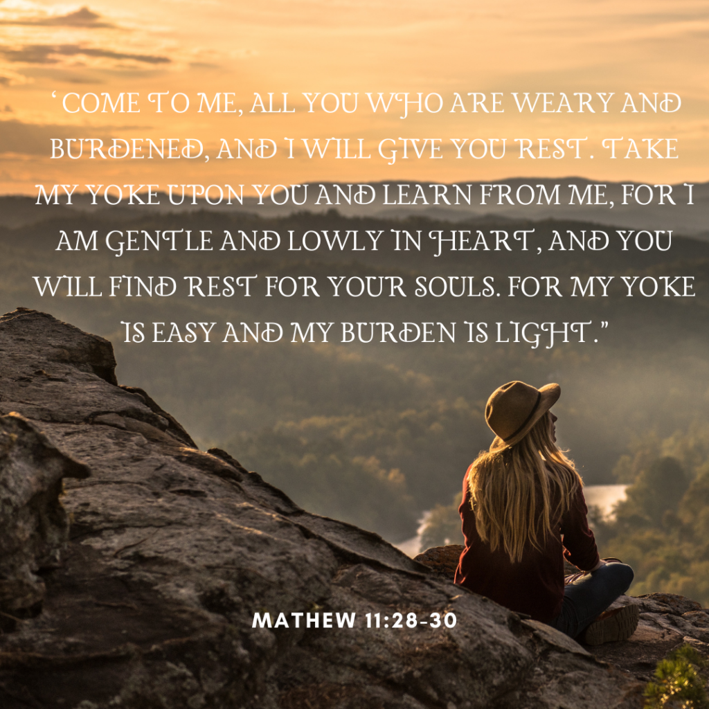 A young woman with long blonde hair wearing a brown hat sits on a rocky cliffside, looking out over a vast, misty forest valley at sunset. Overlaid on the warm, golden sky is the Bible verse Matthew 11:28-30: “Come to me, all you who are weary and burdened, and I will give you rest...” written in a white, elegant serif font.
