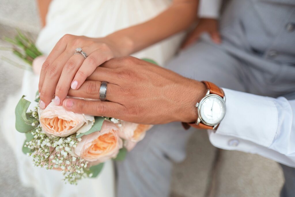 Close-up of a married couple holding hands with wedding rings and a bouquet, symbolizing love, marriage, and lifelong commitment grounded in faith.