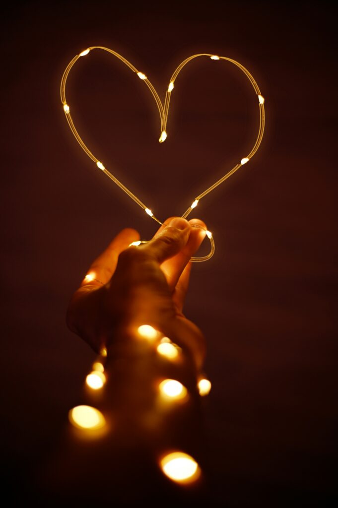 A hand holding glowing string lights shaped like a heart, symbolizing warmth, devotion, and the light of God’s love found in Bible verses about love in a relationship